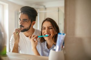 A couple brushing their teeth together while looking in a mirror