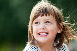 Young girl looking off into the distance, smiling with all of her baby teeth