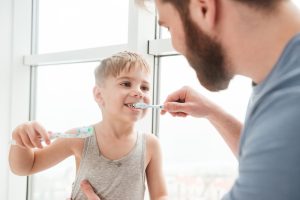 A young father helping his son to brush his teeth.
