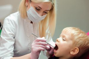 A dental hygienist examining a child's teeth with a scaler tool.