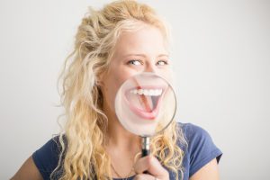 A blonde young adult woman that is smiling and holding up a magnifying glass in front of her mouth.