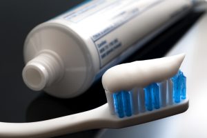 An image of a toothbrush with toothpaste on it. The toothpaste tube is in the background.