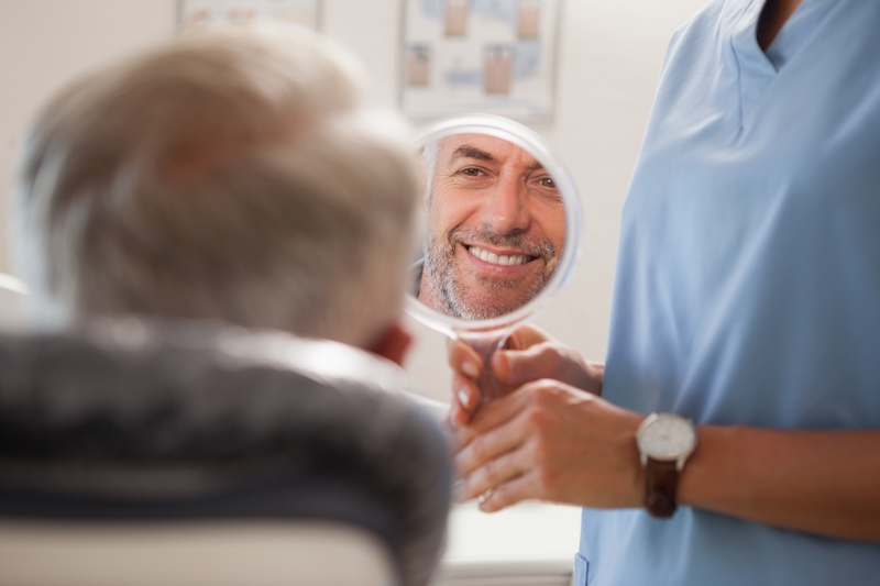 Man looking into a mirror at his teeth in the dentist office.