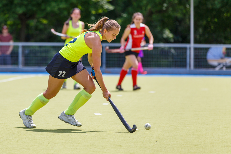 Young female field hockey player handling the ball during a game while others look on.