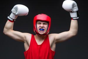 Young teen boy boxer that is holding his arms up in triumph and smiling with a mouthguard in his mouth.