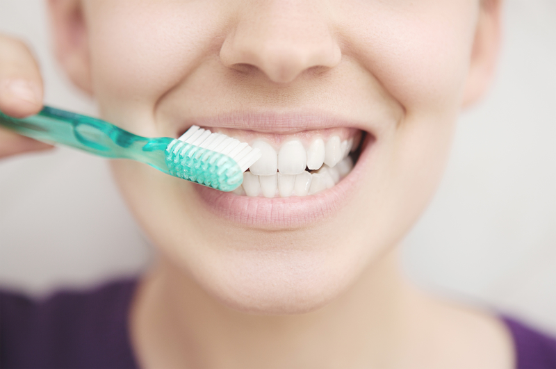Close up view of a woman's mouth as she is brushing her teeth.