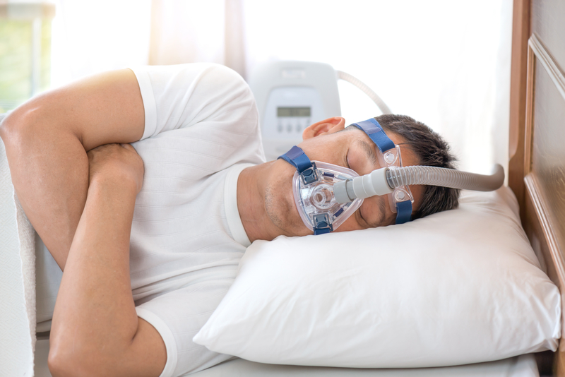 Man sleeping in bed with a CPAP machine on his face for sleep apnea.