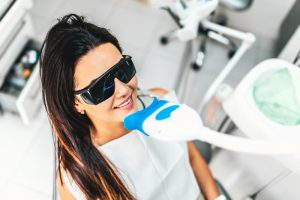 A brunette woman wearing protective glasses as she is about to receive a professional teeth whitening treatment in office.